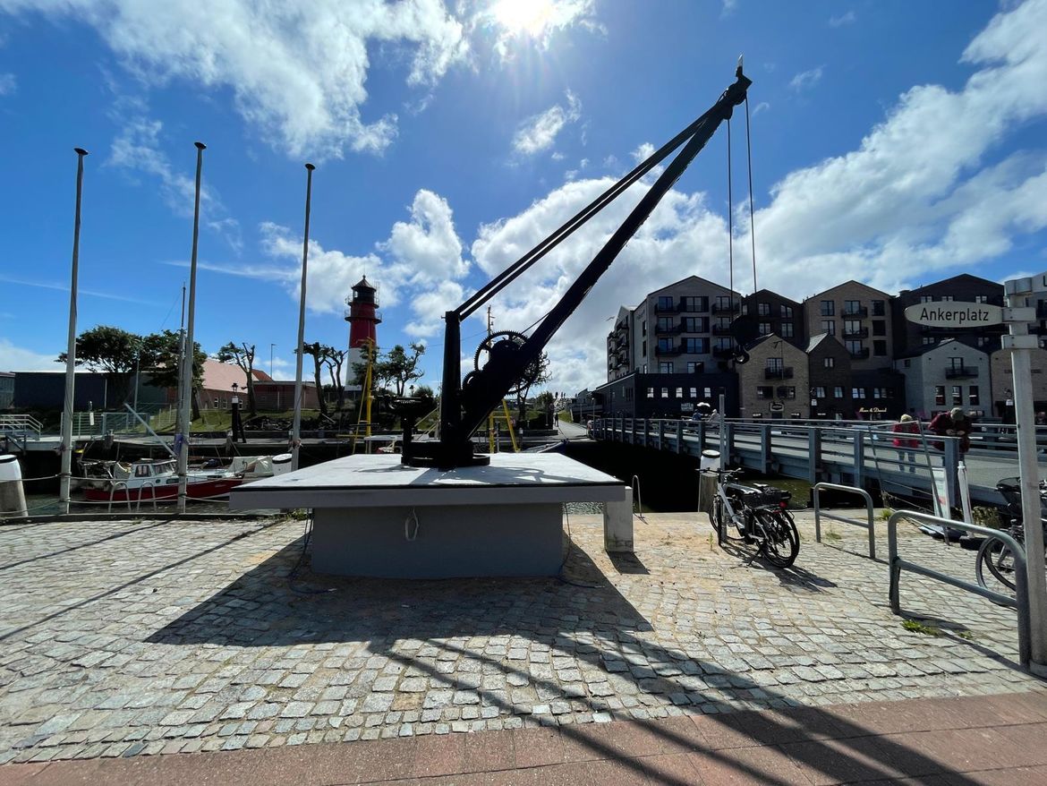 Antiker Kran auf dem Büsumer Ankerplatz mit Museumshafen, Leuchtturm und Hotel Lighthouse im Hintergrund